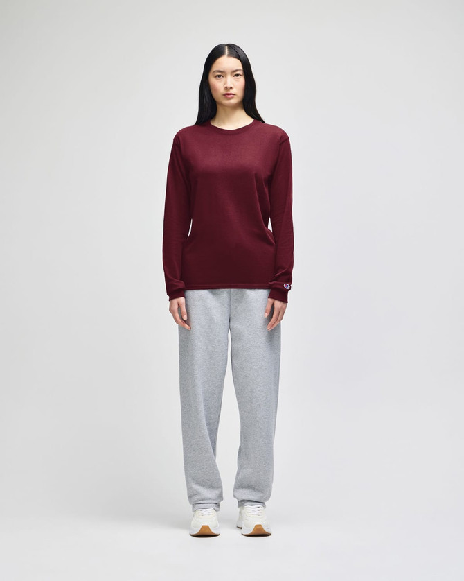 A long-sleeve t-shirt in maroon worn with grey sweatpants. The t-shirt features a logo on the sleeve.