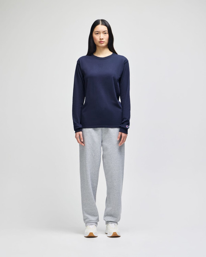 A long-sleeve navy T-shirt displayed on a model paired with grey sweatpants and white sneakers. The shirt features a logo.