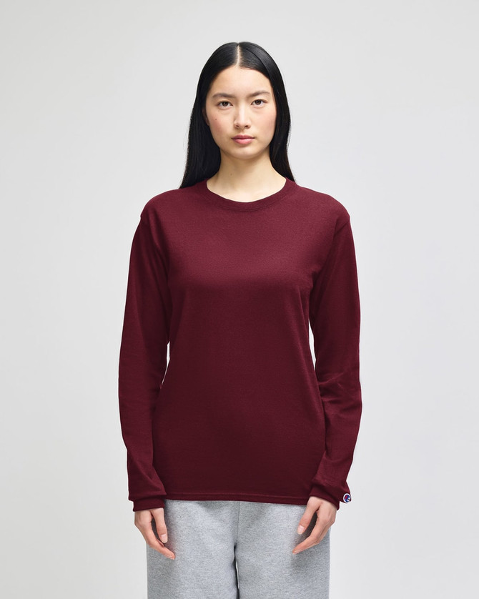A maroon long-sleeve t-shirt on a model, featuring a logo on the sleeve and paired with grey pants.