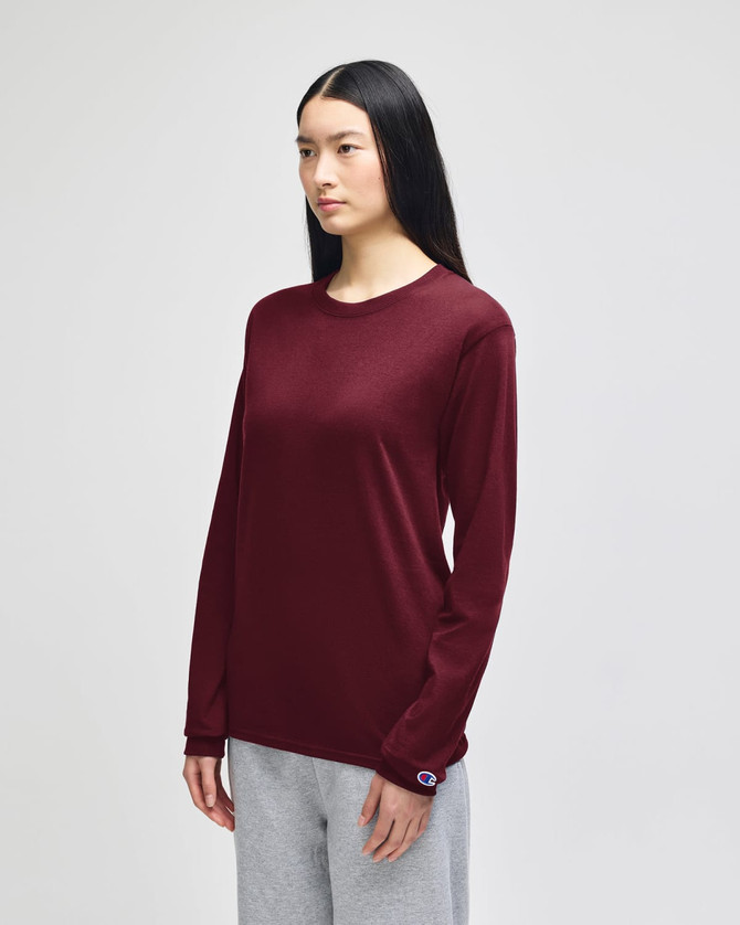 A maroon long-sleeve t-shirt worn by a model, paired with grey pants. The shirt features a logo.