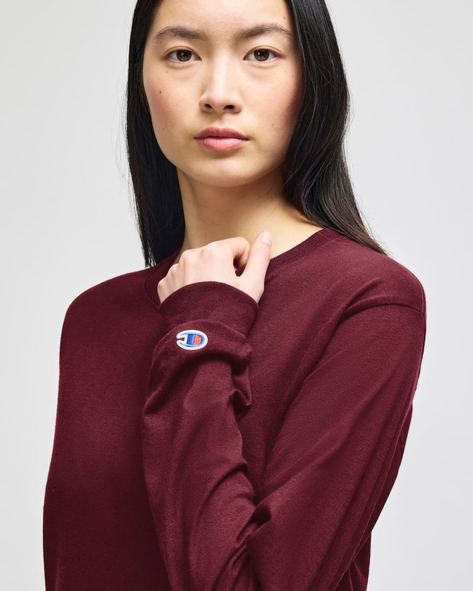A maroon long-sleeve t-shirt with a branding logo on the sleeve. The model is facing forward.