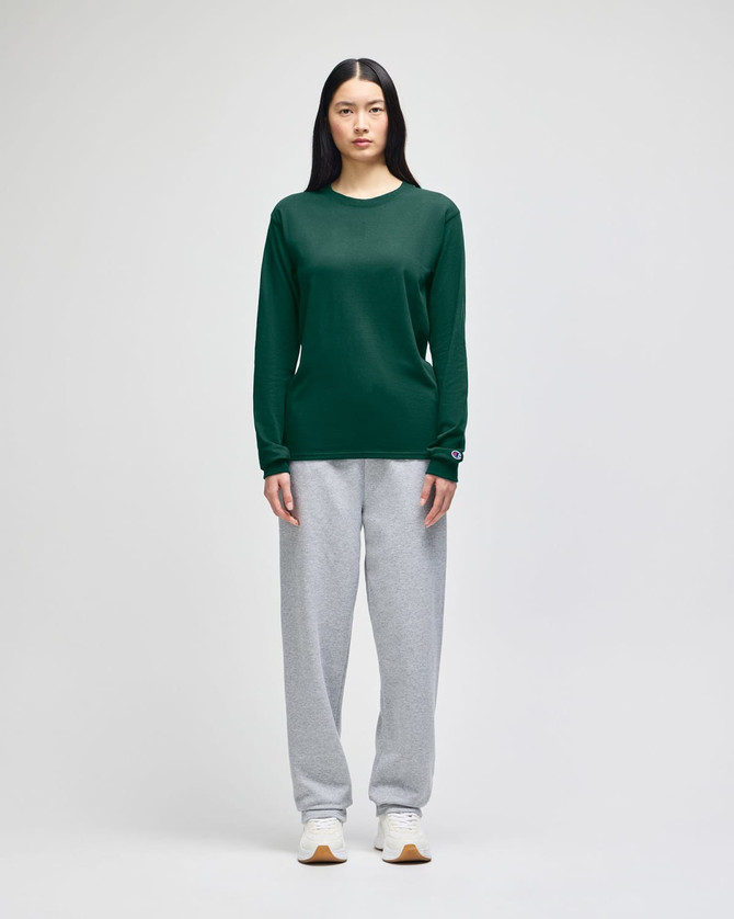 A long-sleeve green t-shirt worn with grey sweatpants. The t-shirt features a logo on the sleeve.