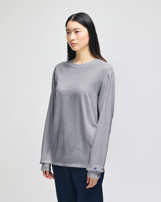 A grey Champion adult long-sleeve t-shirt displayed on a model, featuring a logo on the sleeve.