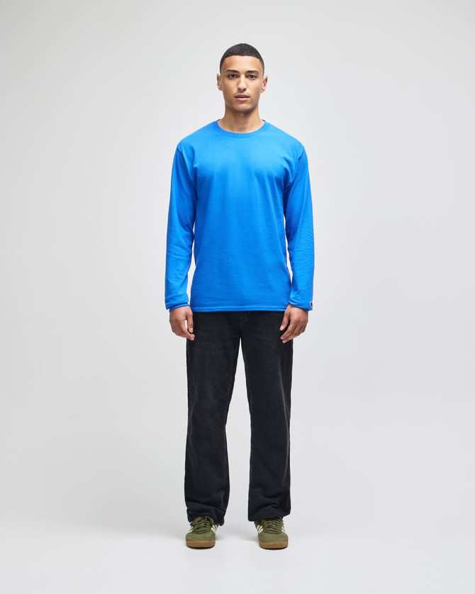 A blue long-sleeve T-shirt worn by a model, paired with black pants and green shoes. The product has a logo.