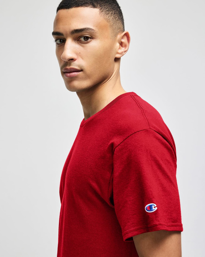 A man wearing a red Champion adult jersey short sleeve t-shirt, featuring a logo on the sleeve.