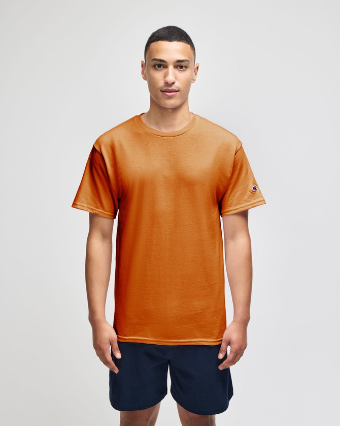 An orange short sleeve T-shirt with a logo, modelled by a person wearing navy shorts.