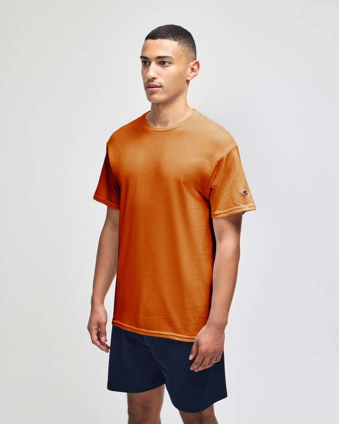 An orange short sleeve t-shirt with a logo, paired with navy shorts, worn by a model.