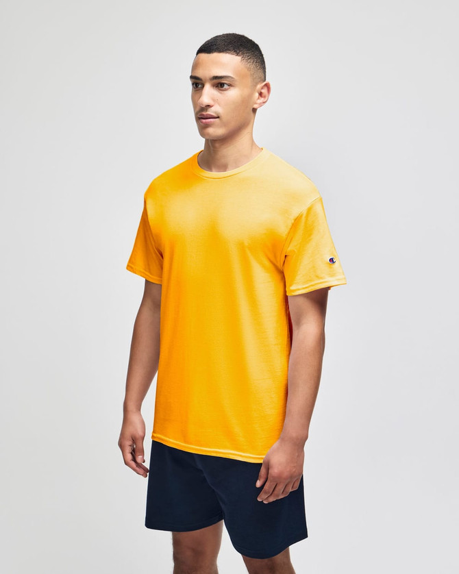 A yellow short sleeve t-shirt with a logo, worn by a model, paired with navy shorts.