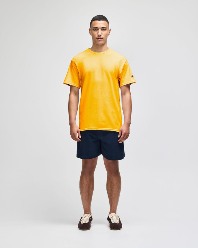A yellow short sleeve t-shirt worn by a model, paired with navy shorts. The shirt features a small logo.