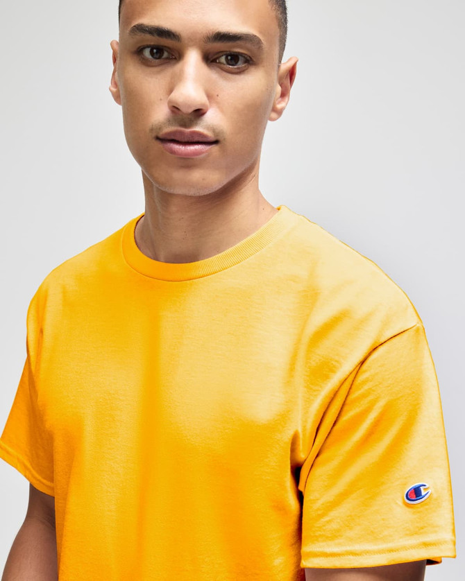 A yellow short sleeve t-shirt featuring a logo on the sleeve, worn by a model.