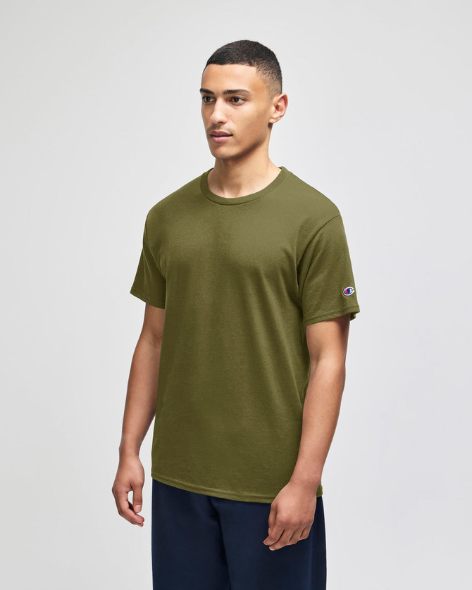 A green Champion adult jersey short sleeve T-shirt displayed on a model, featuring a logo on the sleeve.