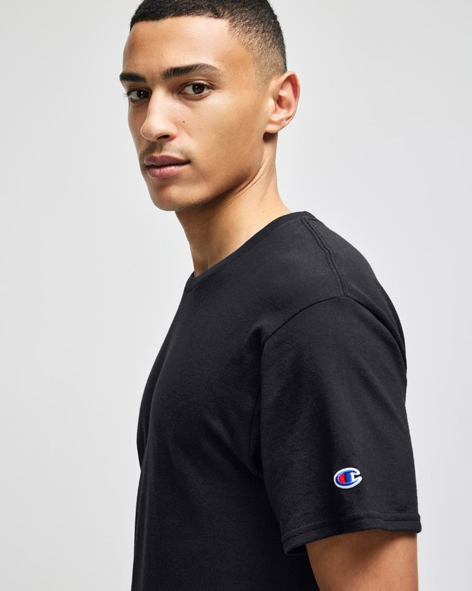 A black Champion adult jersey short sleeve t-shirt with a logo on the sleeve, worn by a model.