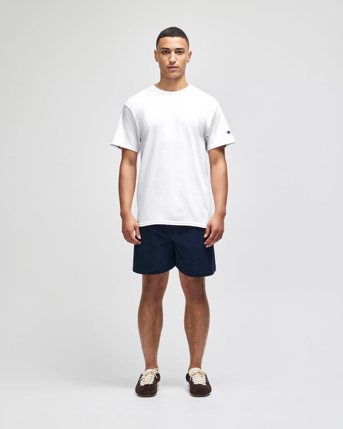 A plain white short sleeve t-shirt with a logo, worn with navy blue shorts.