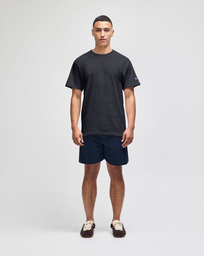 A model stands wearing a grey short sleeve t-shirt and navy shorts, featuring a logo on the shirt.