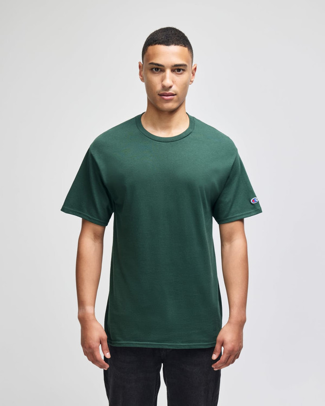 A green Champion adult jersey short sleeve T-shirt displayed on a model, featuring a logo on the sleeve.