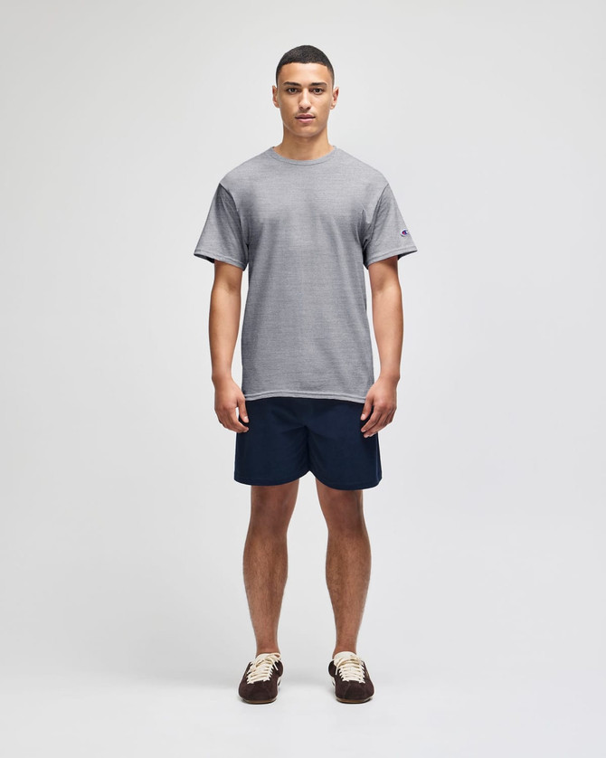 A model wearing a grey short sleeve t-shirt and navy shorts, featuring a logo on the t-shirt.