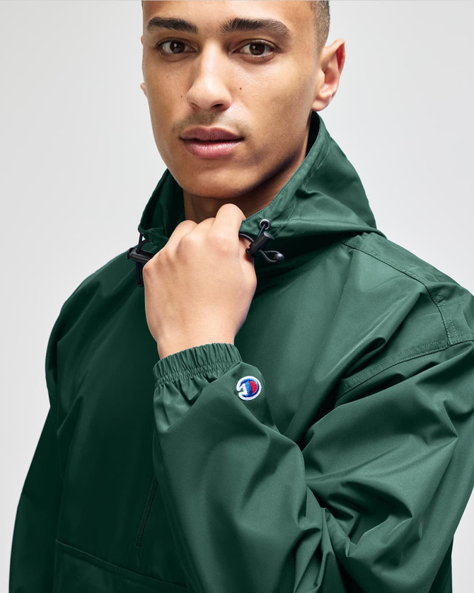 A man wearing a green Champion packable anorak jacket with a hood, featuring a logo on the sleeve.