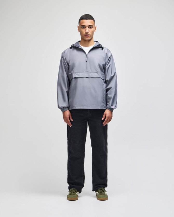 A packable anorak jacket in grey, featuring a half-zip closure and a logo, displayed by a model wearing black pants.