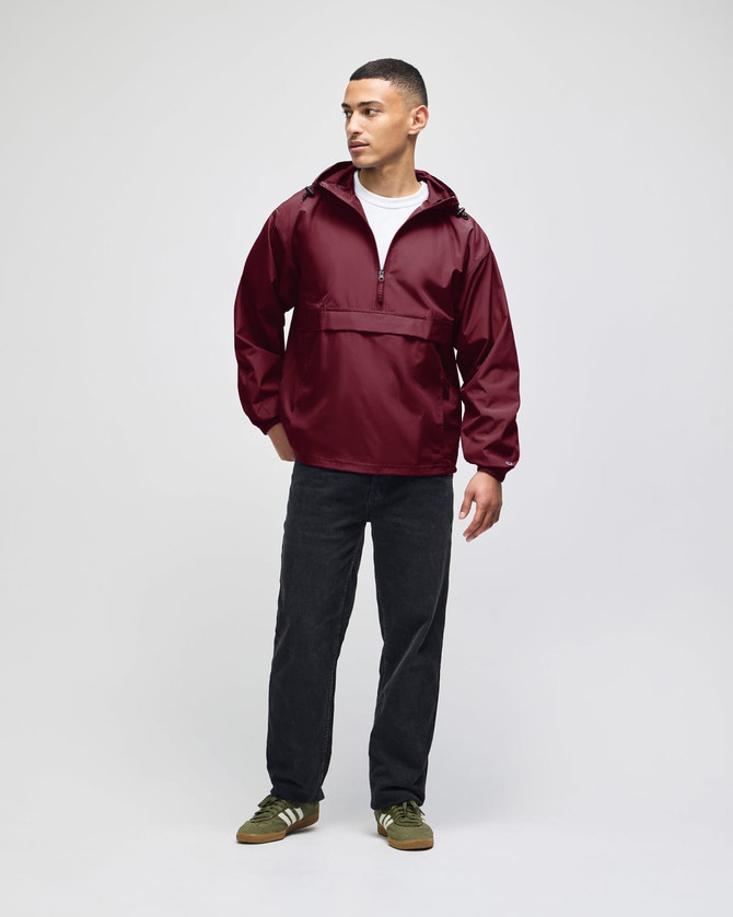 A maroon packable anorak jacket with a hood, worn by a model, paired with dark pants and green shoes.