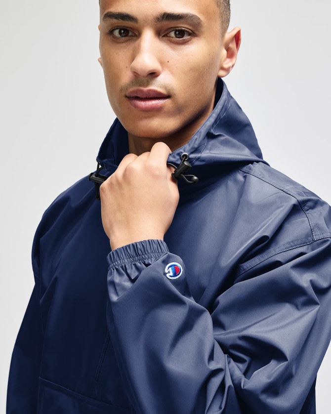 A navy blue packable anorak jacket with a front pocket, featuring a logo on the sleeve.