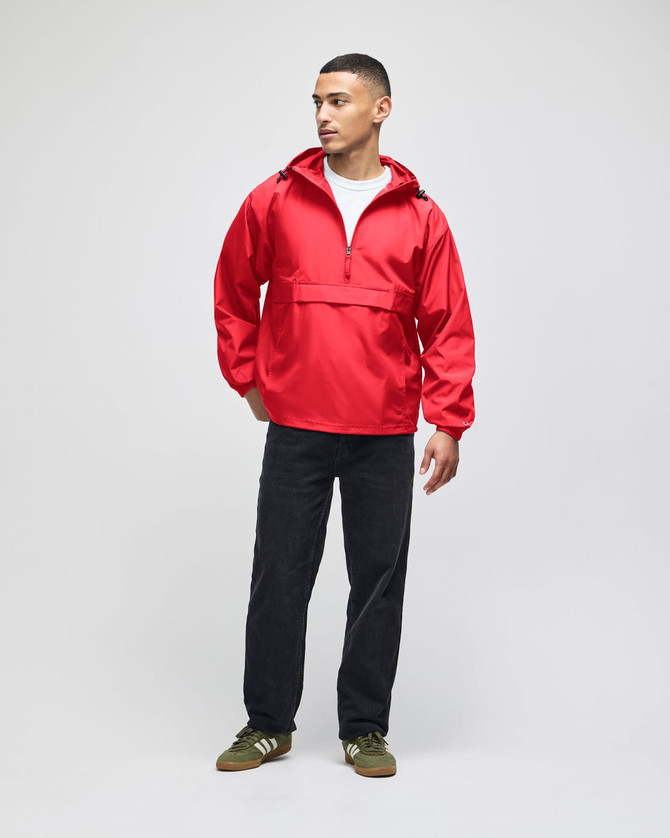 A red packable anorak jacket featured on a model, paired with black pants and green shoes. It has a logo.