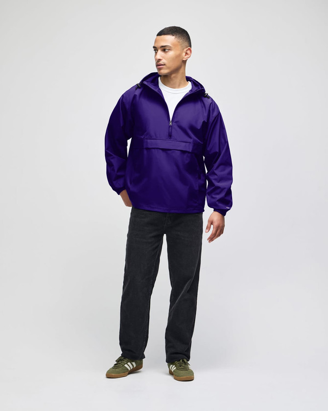 A packable anorak jacket in purple, featuring a hood and front pocket, worn by a model with dark pants and shoes.