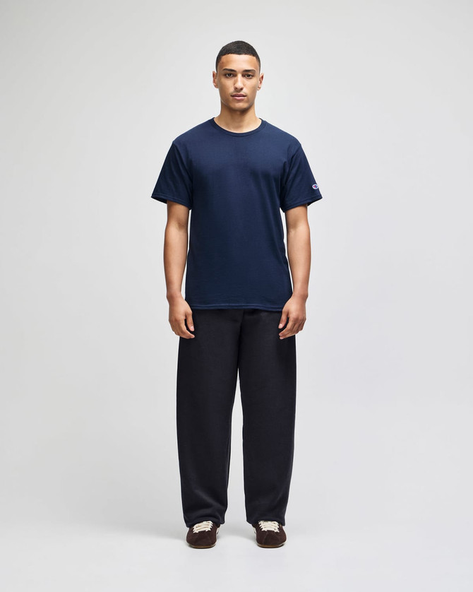 A model stands wearing navy track pants with open bottoms, paired with a matching navy t-shirt. The pants feature pockets.
