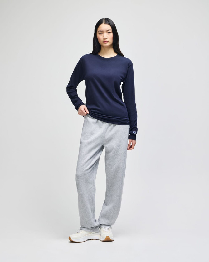 A model stands wearing grey fleece track pants with pockets and a navy long-sleeve top. The outfit includes a logo.