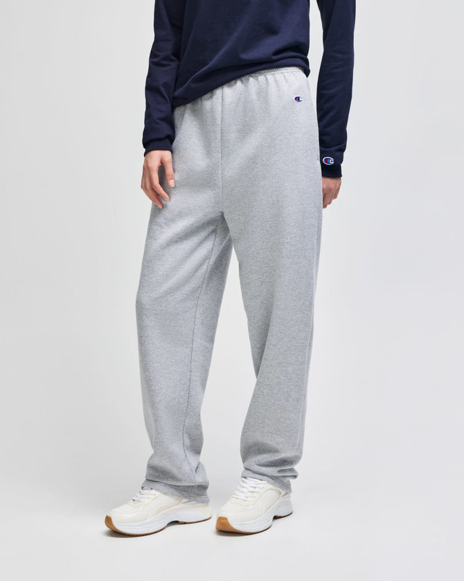 Light grey open-bottom fleece pants with pockets, featuring a logo, styled with a navy long-sleeve top and white trainers.