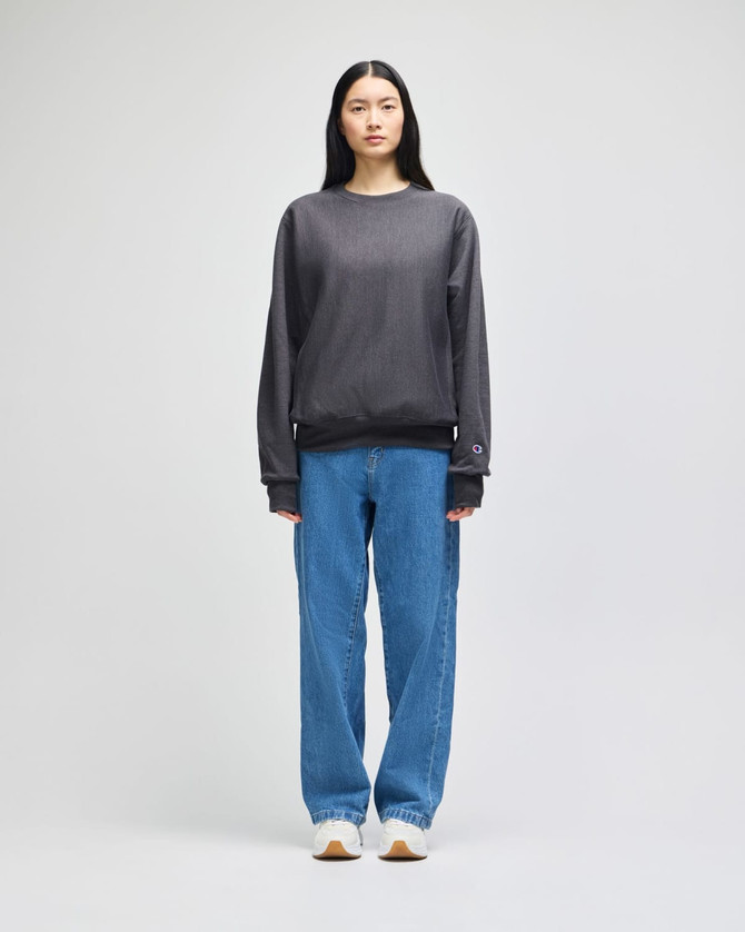 A model wearing a grey cropped hoodie with long sleeves and blue wide-leg jeans, featuring a logo.