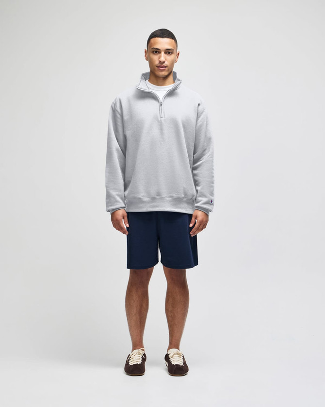 A grey quarter-zip pullover worn with navy shorts, featuring a logo on the sleeve.