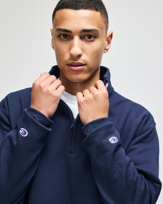 A navy blue quarter-zip pullover featuring a logo on the sleeve, modelled by a young man.