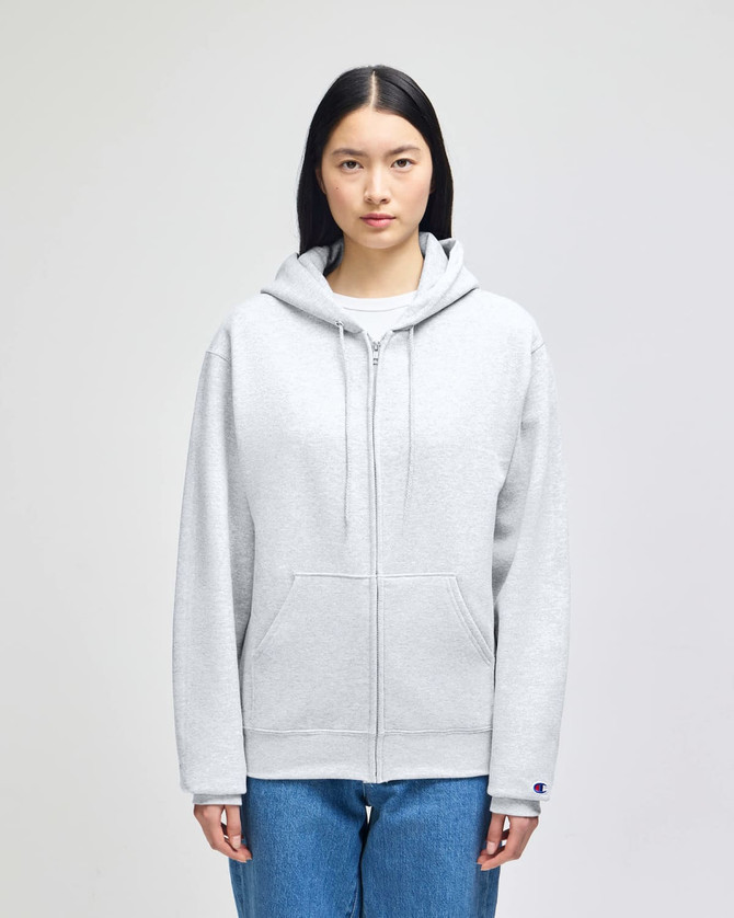A light grey full-zip hooded sweatshirt with a front pocket and a logo on the sleeve, worn by a model.