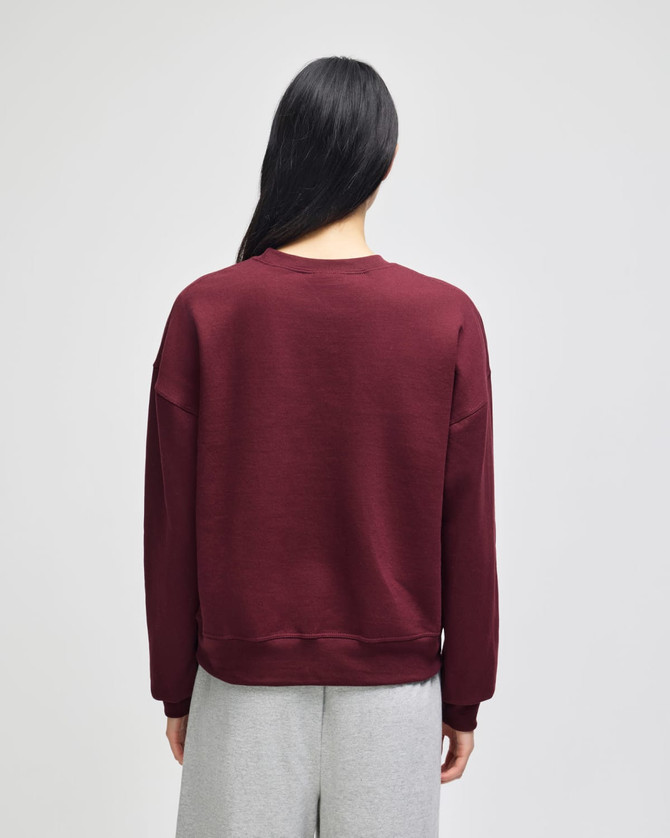 A maroon women's crewneck sweatshirt with a relaxed fit, featuring a branded logo on the back.