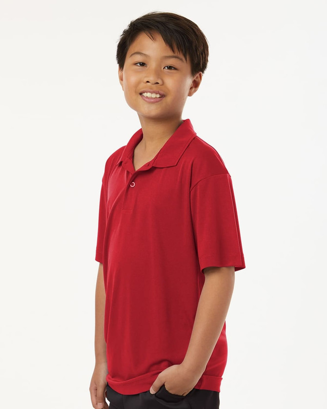 A red polo shirt with a collar, displayed on a smiling young boy in a relaxed pose. The shirt has a logo on it.