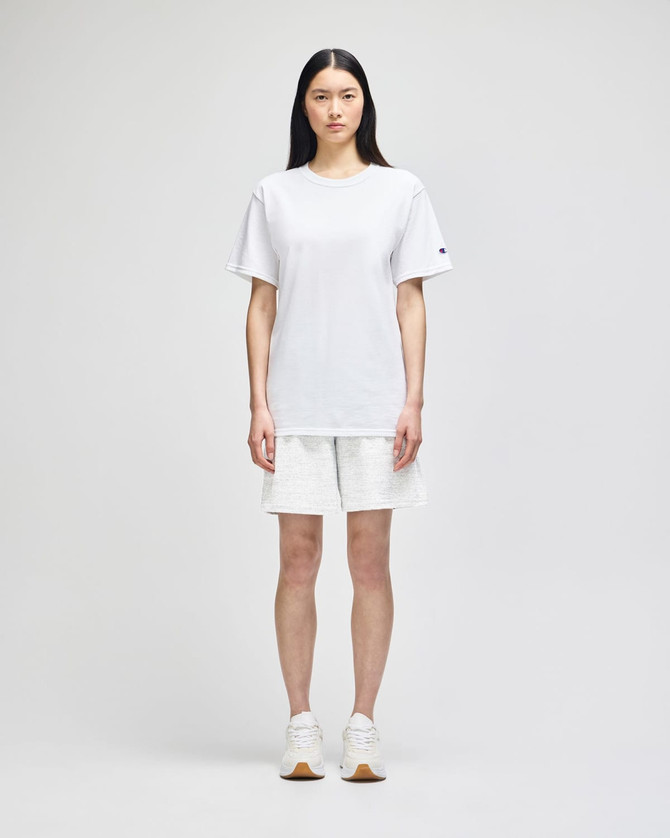 White cotton gym shorts displayed on a model, featuring a logo, paired with a matching white top and white sneakers.