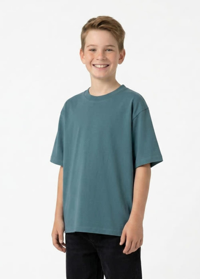A smiling child wearing a faded teal t-shirt made from 100% organic cotton, paired with dark jeans.