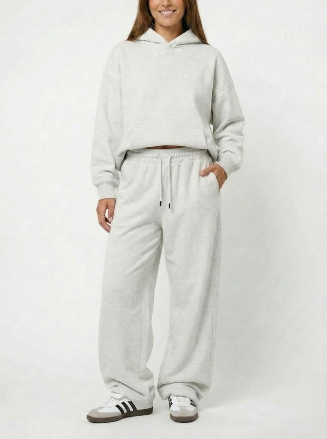 A model wearing unisex wide leg fleece pants in light grey, paired with a matching hoodie. The outfit features a casual style.
