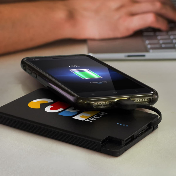 A black power bank with a logo, connected to a phone displaying a charging symbol.