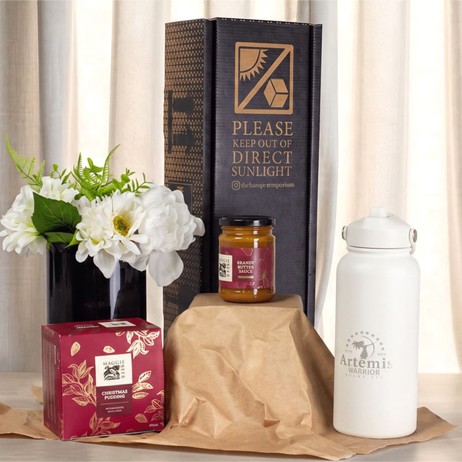 A white drink bottle, a jar of jam, a floral arrangement, and a decorated box, all presented in a festive setting.