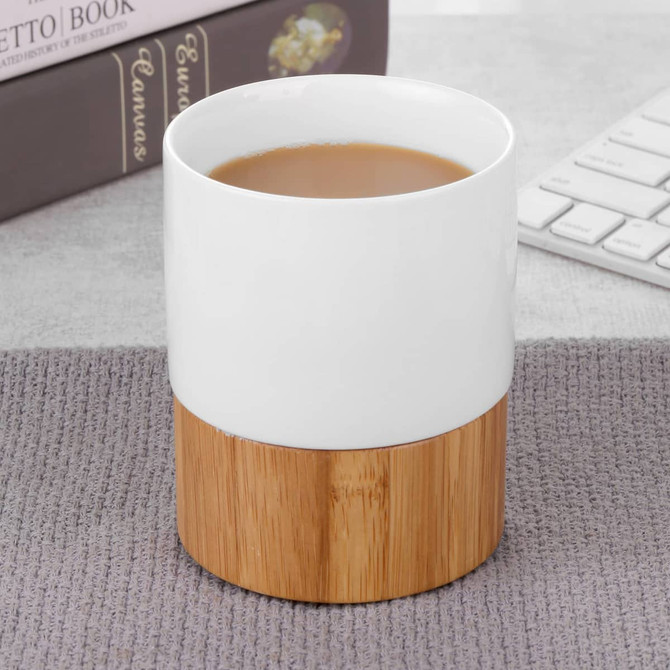 A ceramic mug with a white upper section and a natural bamboo base, filled with a warm beverage.