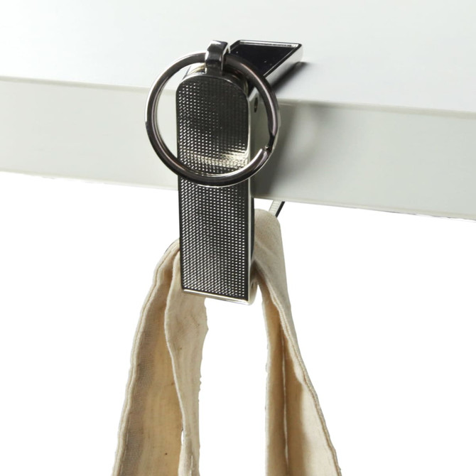 A silver mobile stand and hanger key ring clipped to a flat surface, holding a fabric strap.