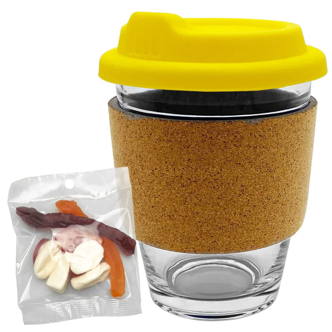A glass coffee cup with a cork band and yellow lid, accompanied by a bag of mixed lollies in various colours.