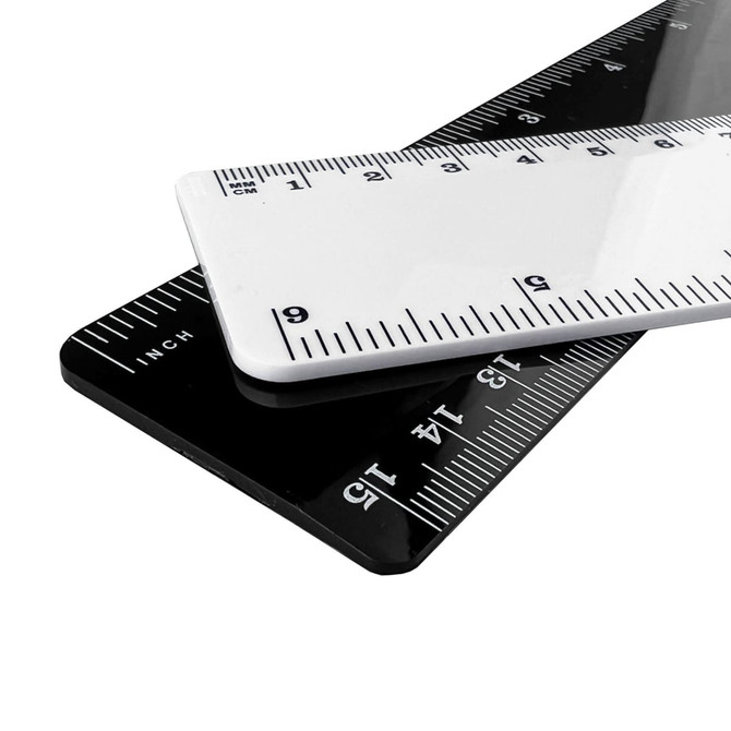 Two plastic rulers, one white and one black, overlapping with measurement markings in both centimetres and inches.