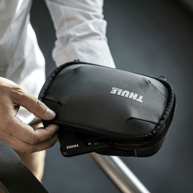 A black Thule Subterra PowerShuttle toiletry bag with a zipped compartment held in a person's hand.