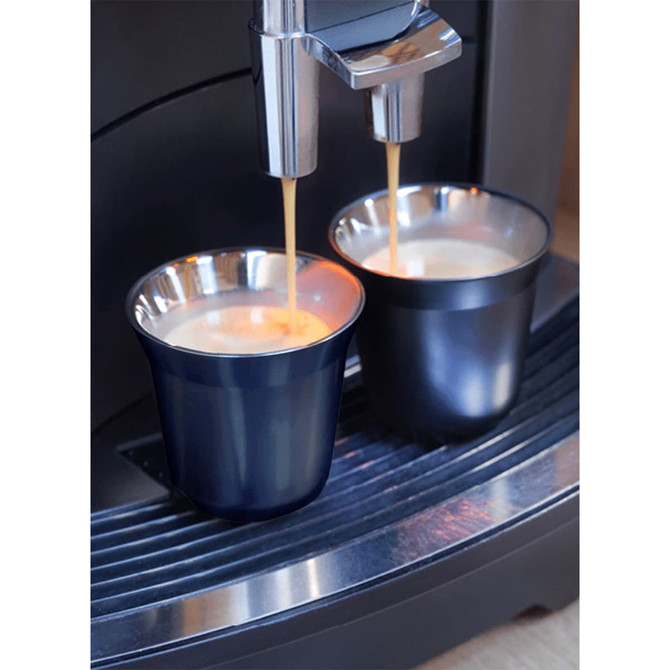 A set of two recycled espresso cups in dark navy, featuring a metallic rim, positioned under a coffee machine.