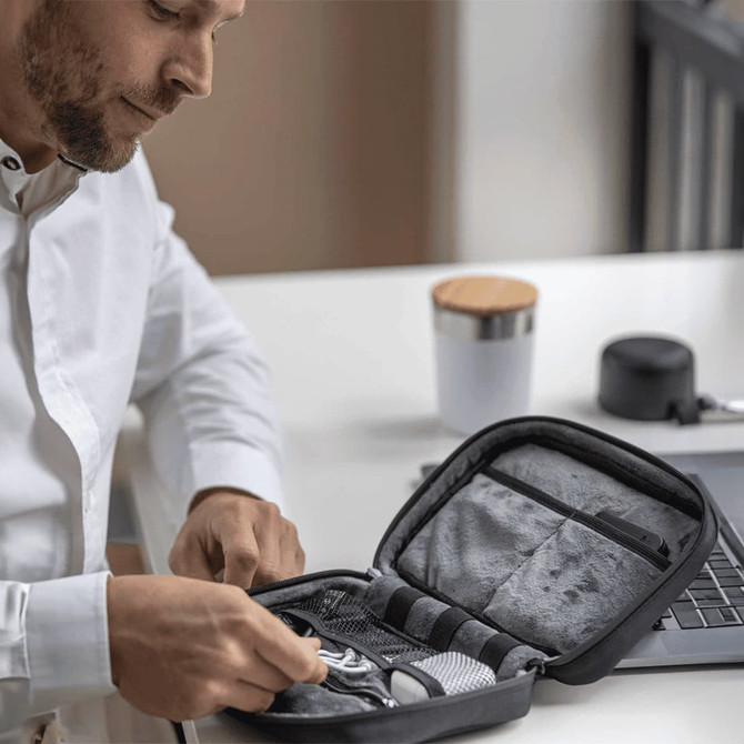 A black organiser pouch with compartments is being opened, revealing various contents on a desk.