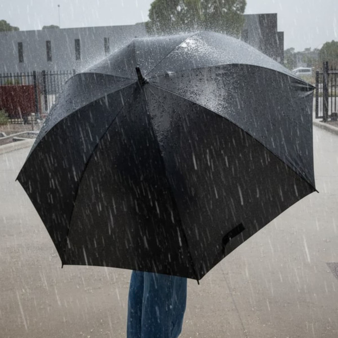 A black umbrella in heavy rain, held by a person wearing blue jeans, with raindrops falling around it.