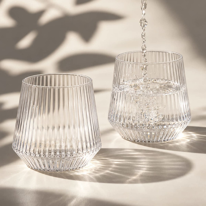 A drink bottle featuring a ribbed design, made of clear glass, with water being poured into two glasses.