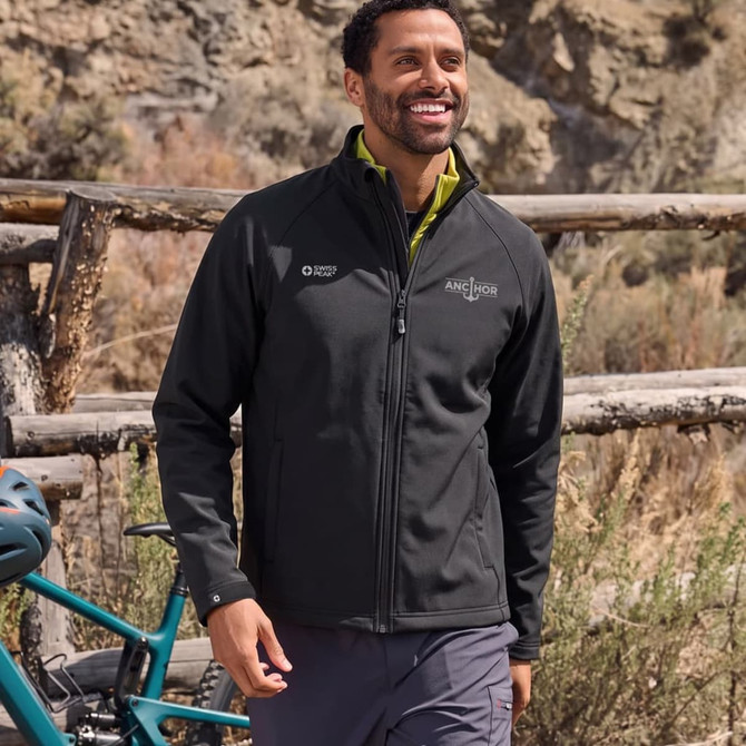 A unisex softshell jacket in black, featuring a logo, worn by a smiling individual outdoors.